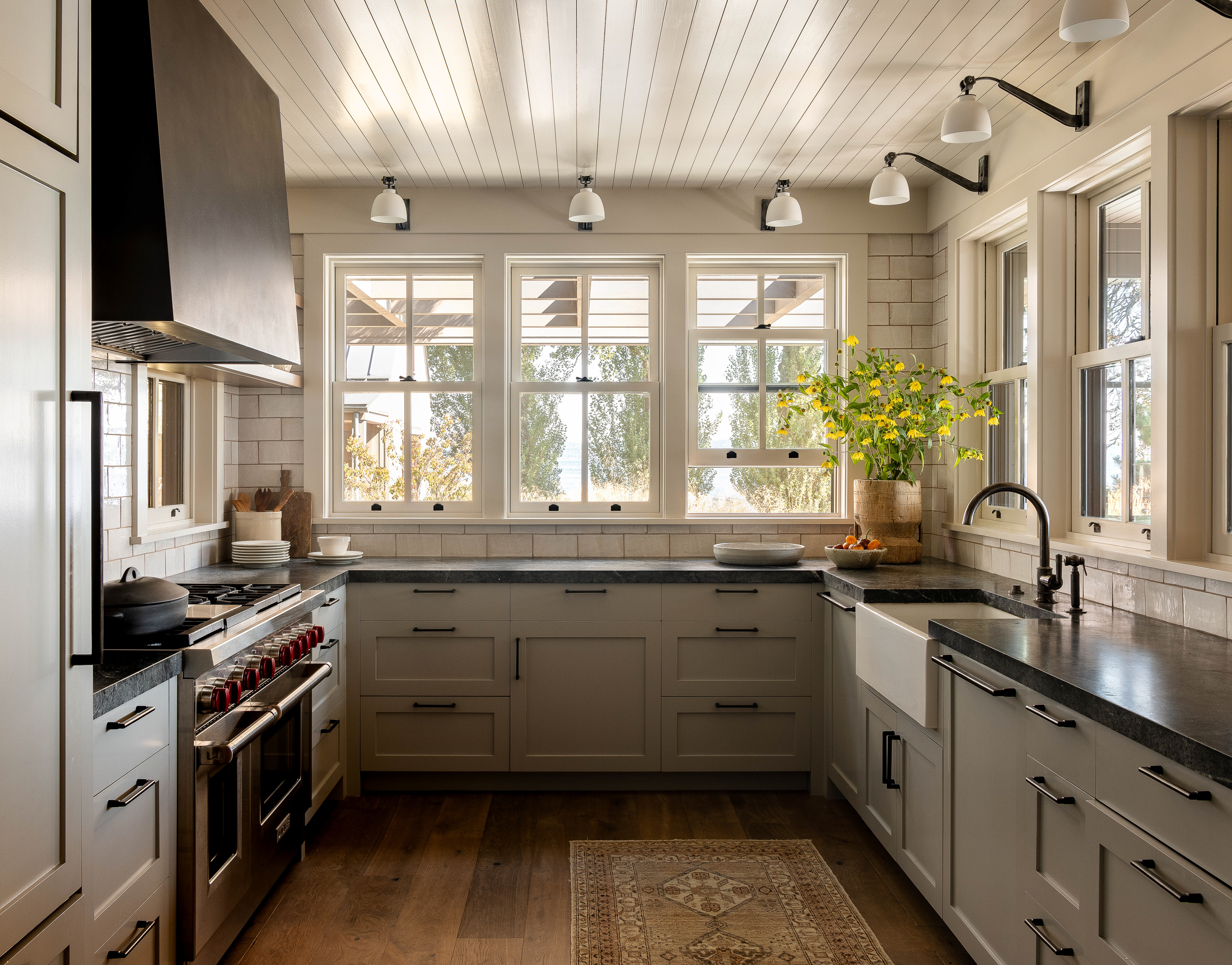 The kitchen features soapstone countertops, brass and bronze fittings, and double-hung windows that offer easy cross ventilation, creating a perfect blend of beach house and farm kitchen vibes.