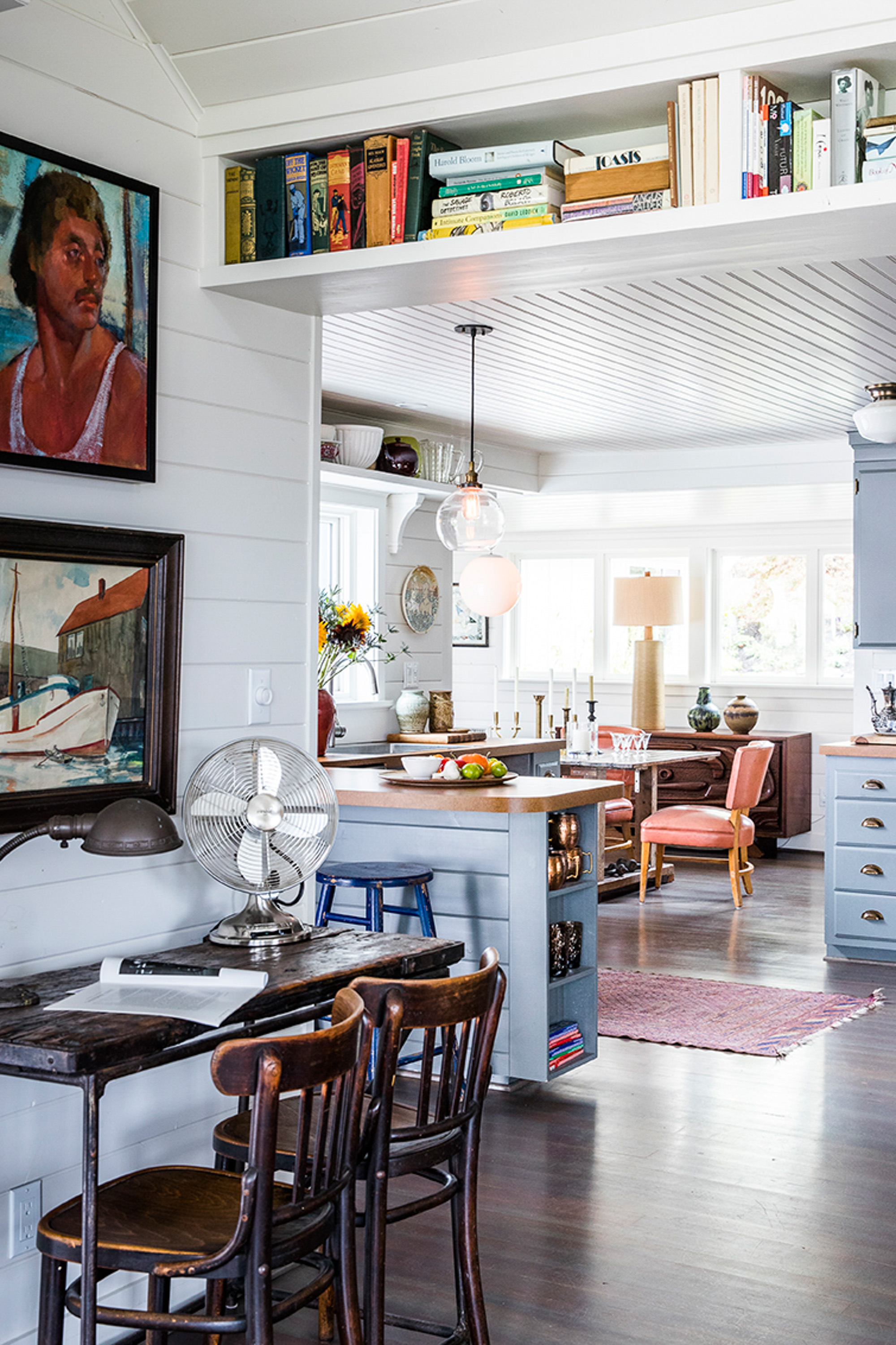 The kitchen retains its 1950s cabinets painted in a gray-blue hue, complemented by aged brass hardware for a sea-captain vibe. Formica countertops offer a nostalgic nod to old beach cottages.