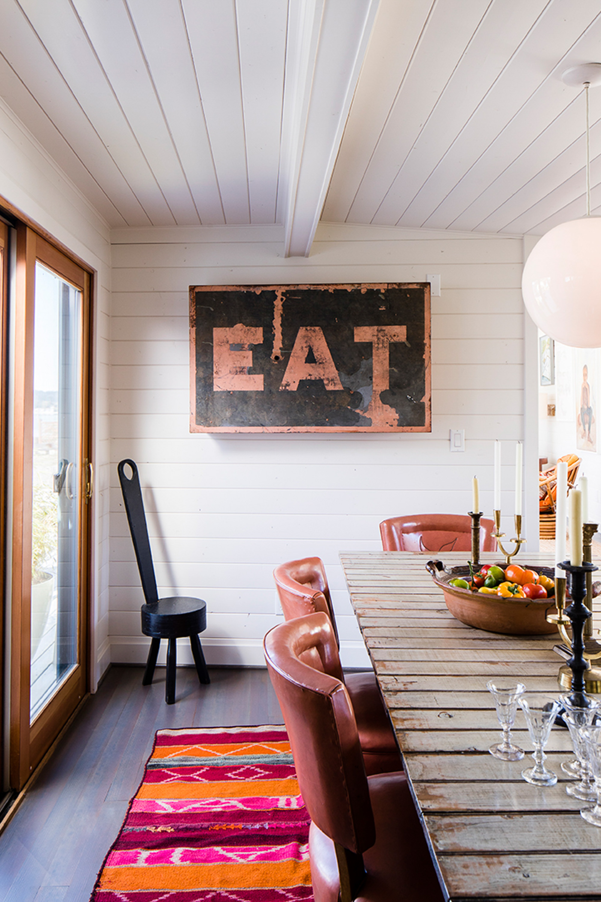 The dining area is a blend of old and new, featuring a weathered dining table crafted with salvaged barn wood, complemented by an EAT sign for added charm.
