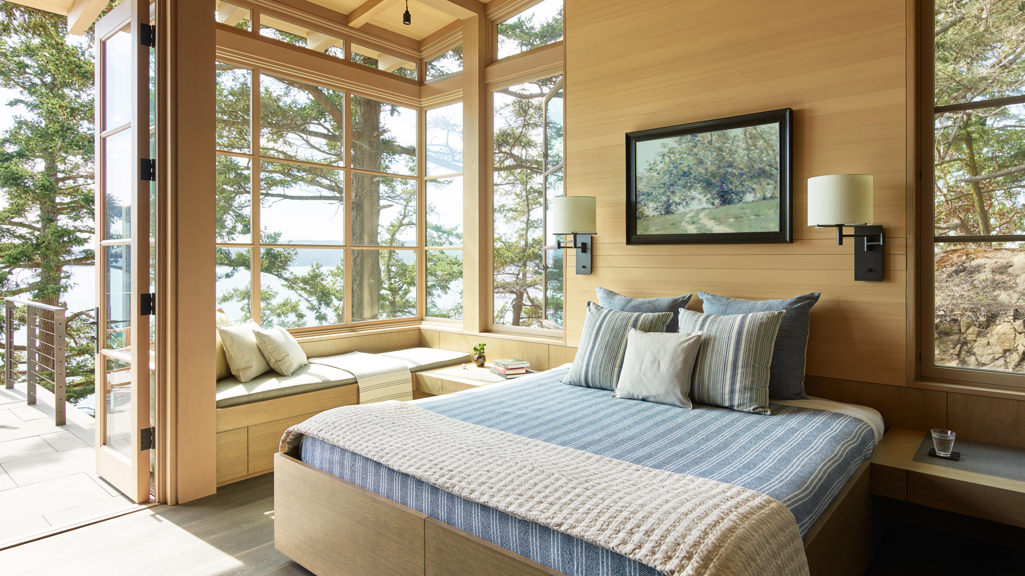 The primary bedroom features warm wood paneling, a built-in window seat, and access to the patio. The room feels warm and inviting with its wood and glass elements.