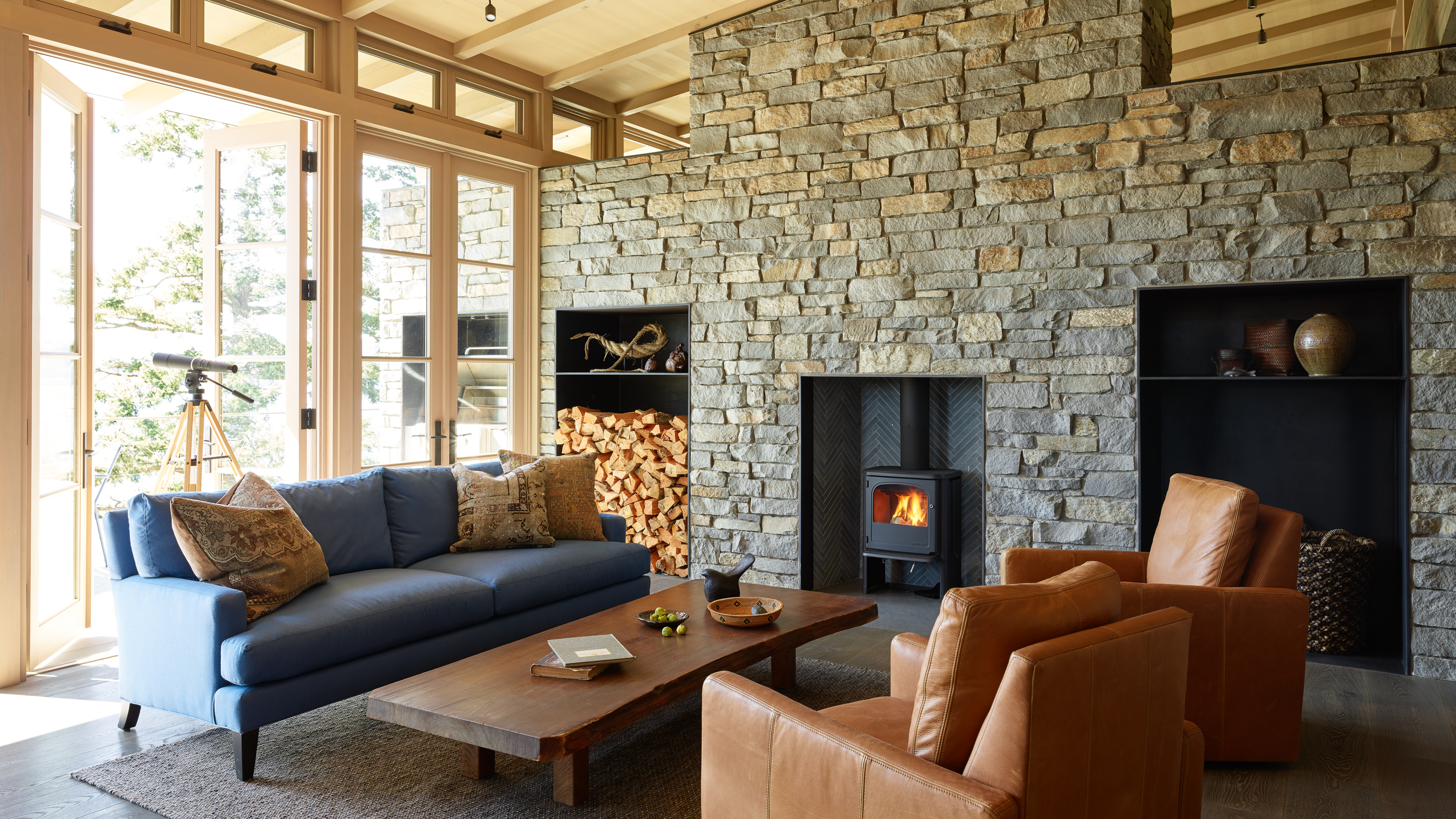 The public area features the wood stove, which is set within a stone wall that mimics the exterior cladding. Stone wraps other walls within the home, helping draw a connection to the natural setting.