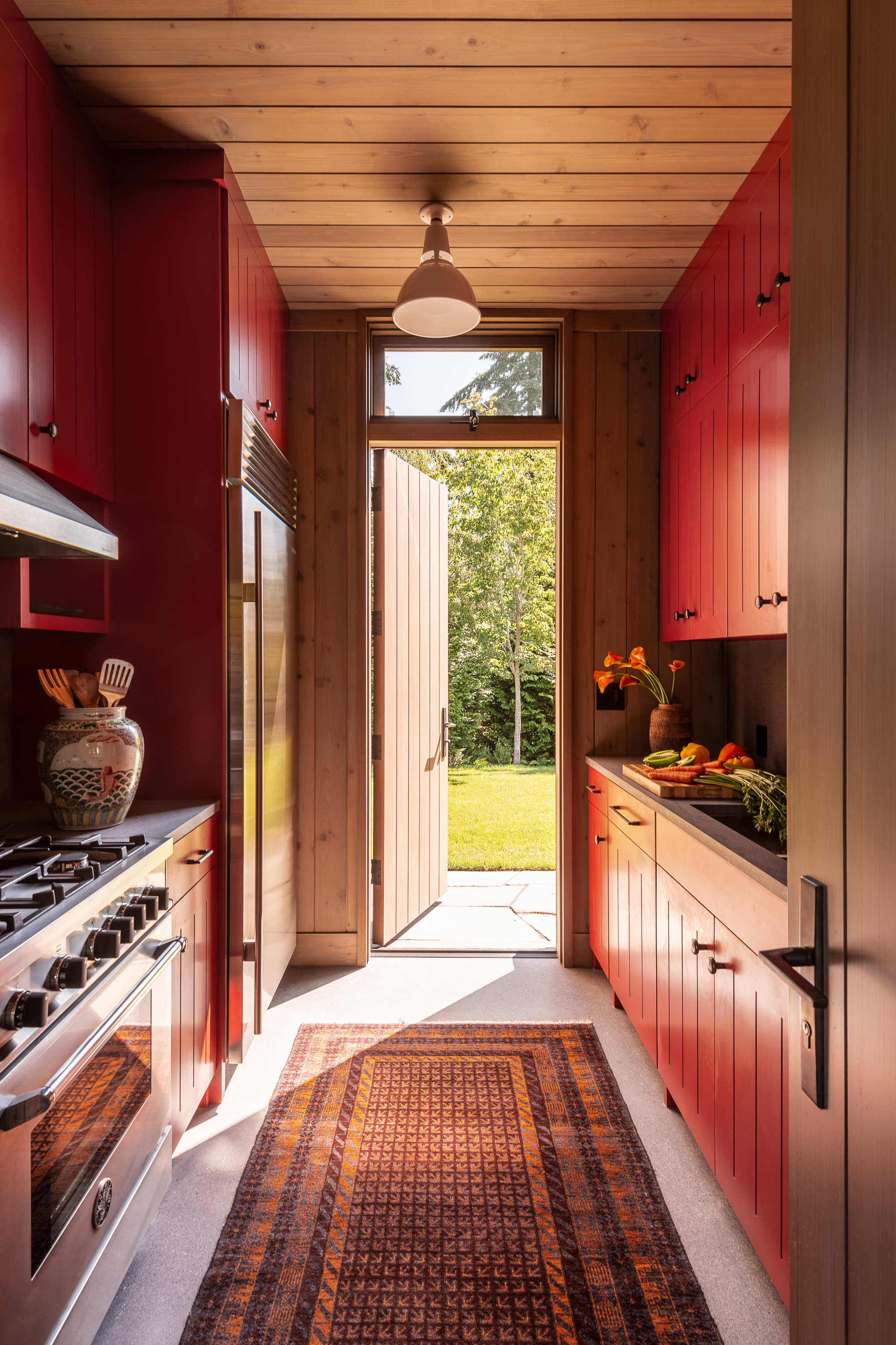 The galley-style kitchen in the Whidbey Island Field House features bold red cabinet paint, adding a vibrant touch to the space.