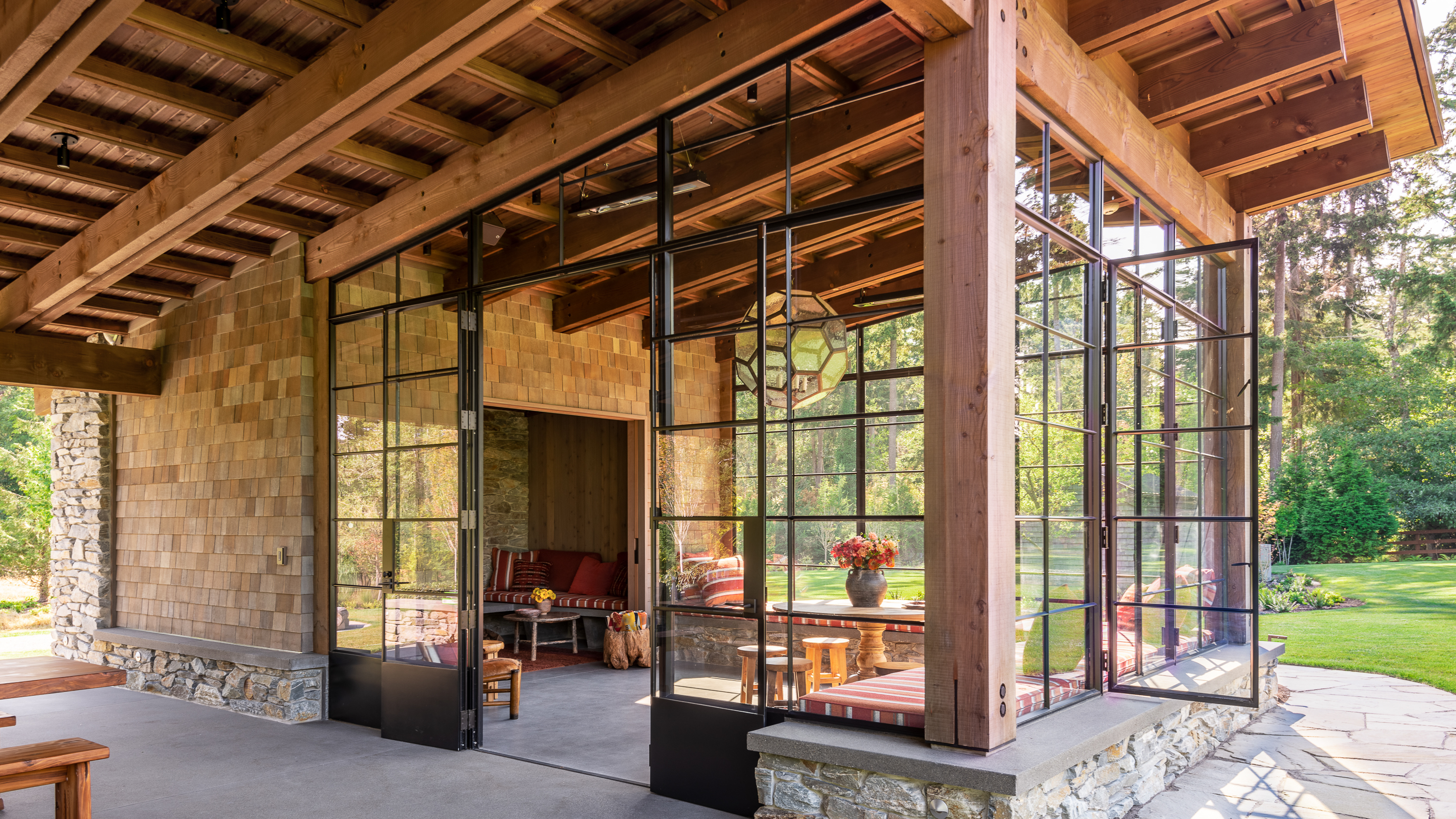 Glass, Timber, and Stone give this indoor/outdoor living space a close connection with nature. Vibrant red textiles bring warmth to the space.