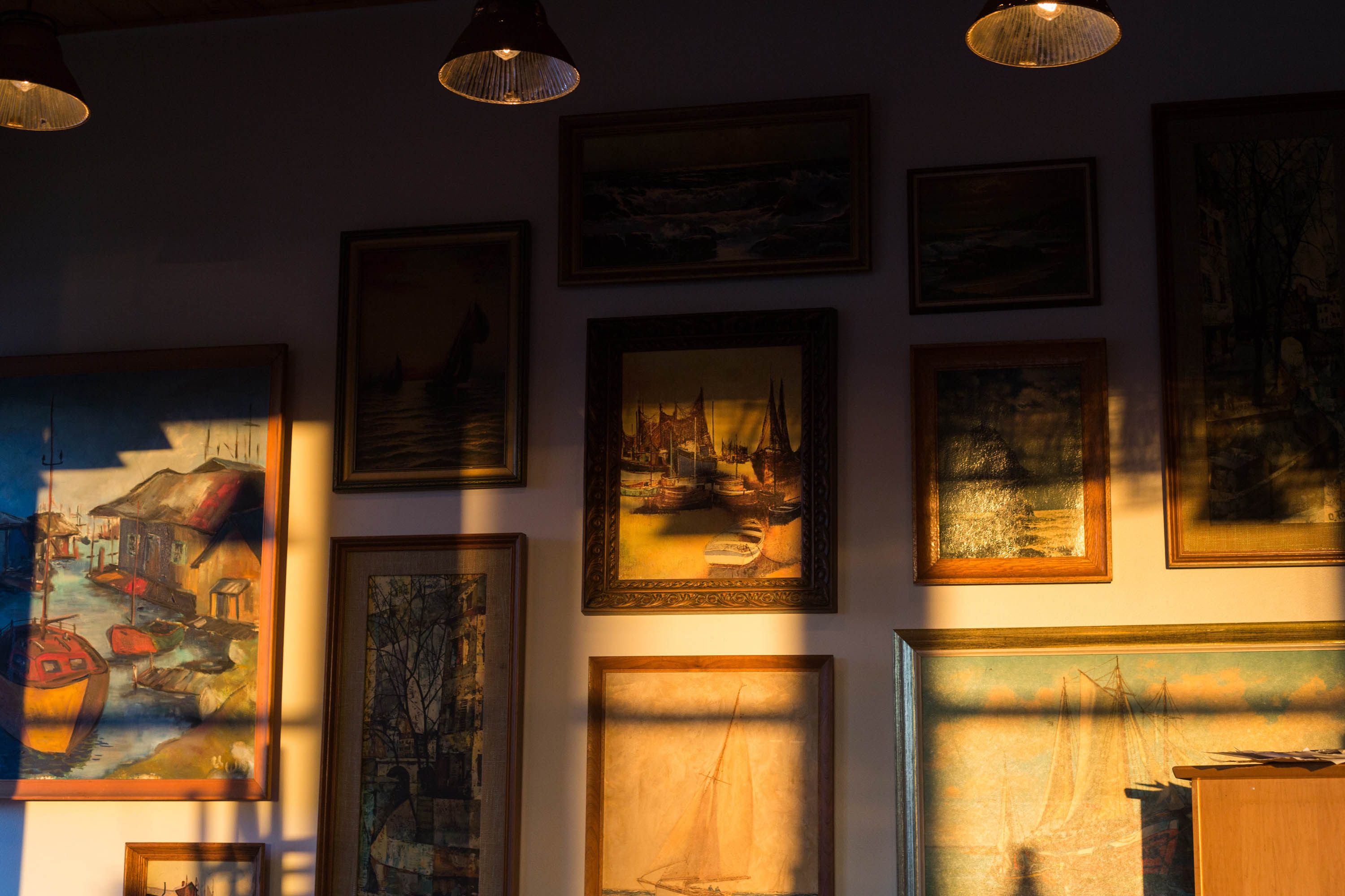 The gallery wall is illuminated by the golden hour light, enhancing the appeal of the paintings.