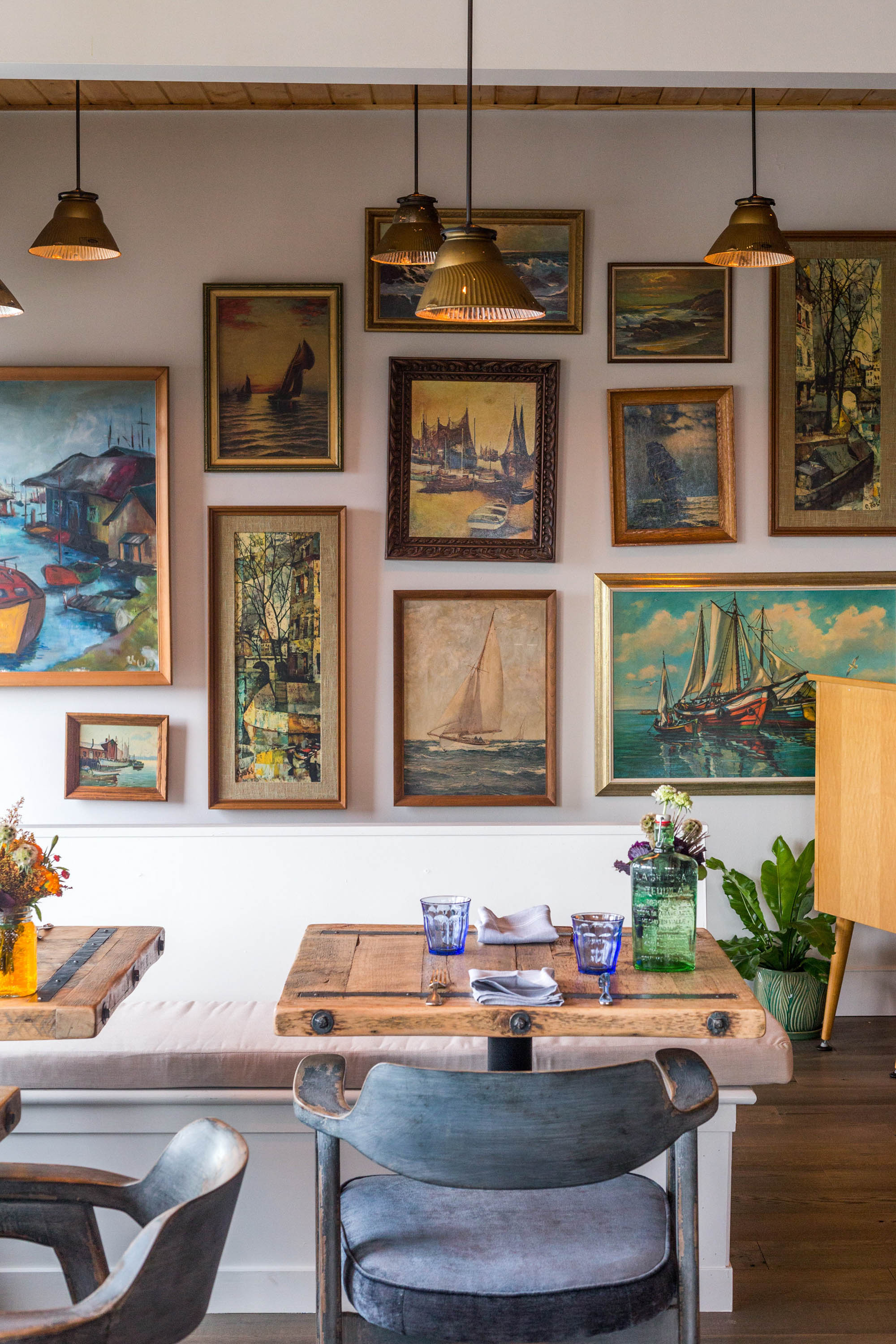 The Gallery Wall near the entrance features classic paintings capturing Alki Beach's essence. Antique gold frames and distressed pendants add warmth.