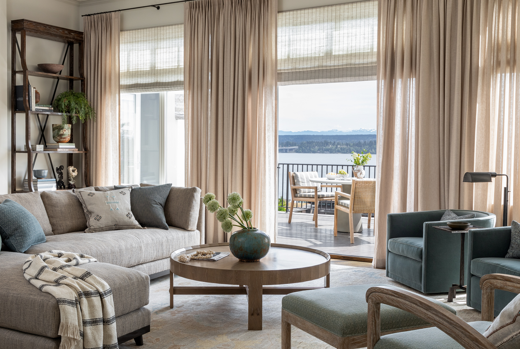 The living room features warm woods, cool gray and blue upholstery, and a view of Lake Washington. A deep brown bookshelf adds a touch of masculine energy to the light, airy space.