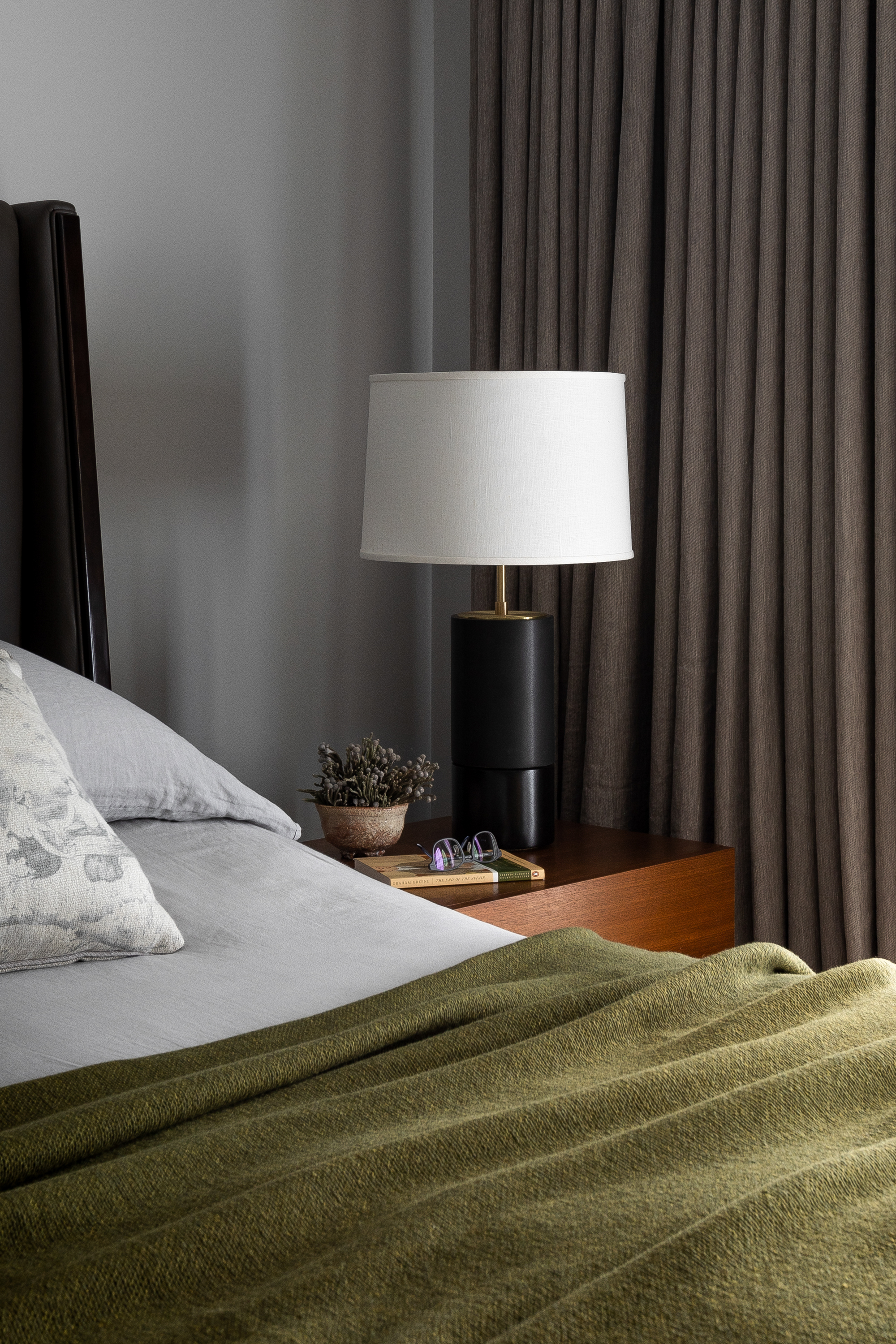 Close-up of the nightstand featuring a modern matte black ceramic lamp with a brass finish.