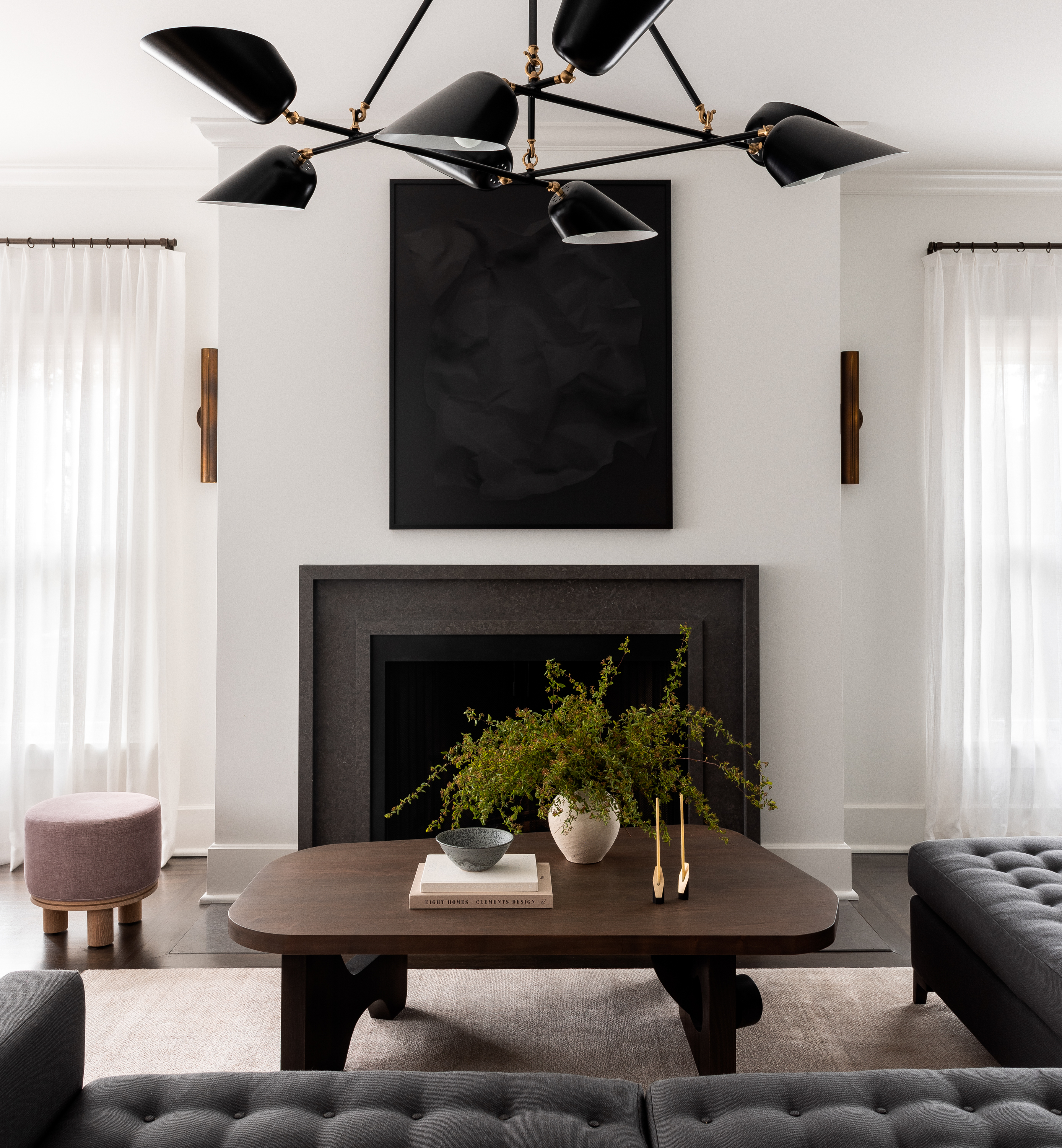 View of the fireplace in the Lake Park Residence renovation, featuring a charcoal-colored stone surround. Many items in this shot are black and charcoal, besides the white walls and white antique rug.