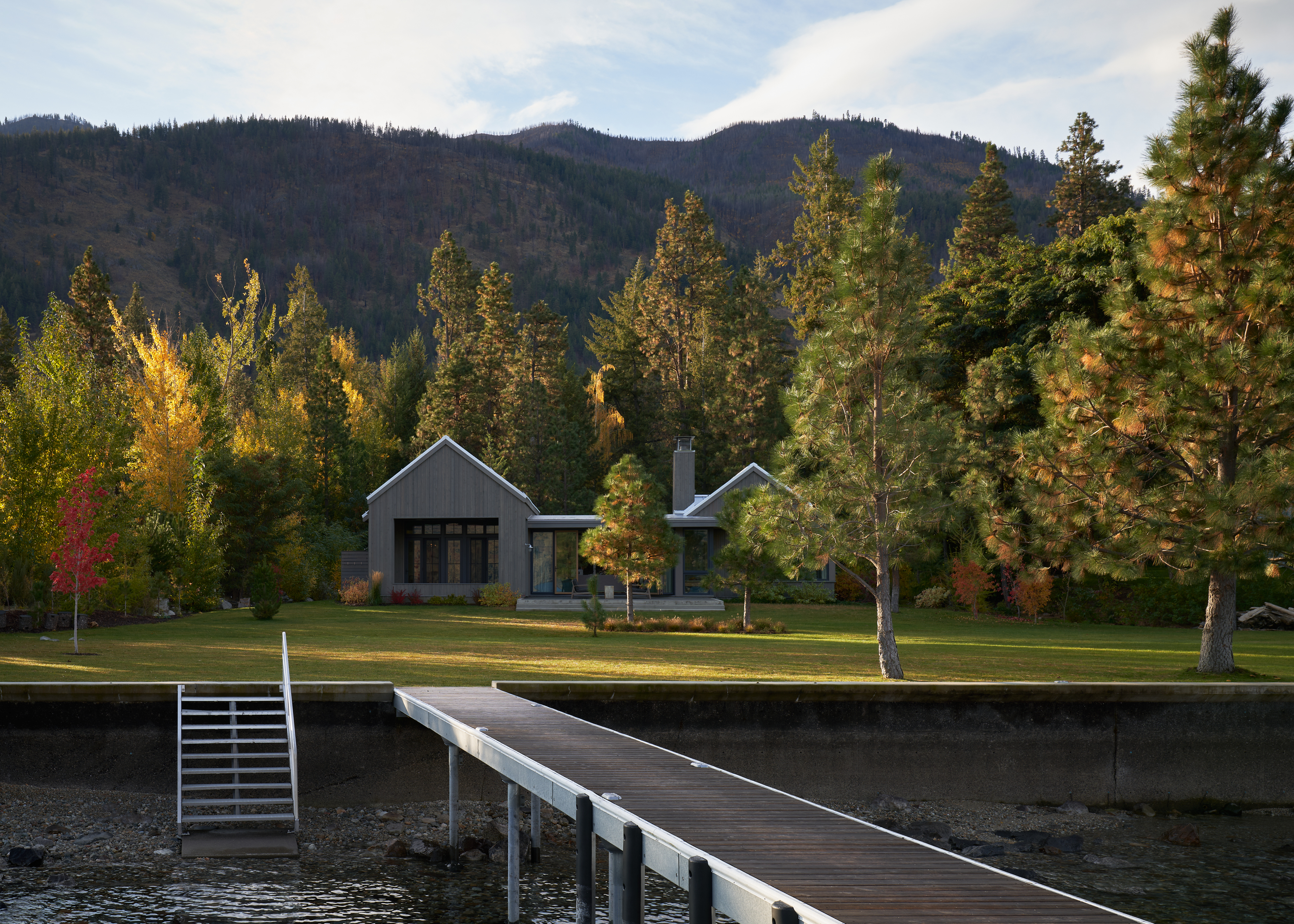 Backyard view of the house by the water with a visible dock. The architecture features clean, simple volumes.