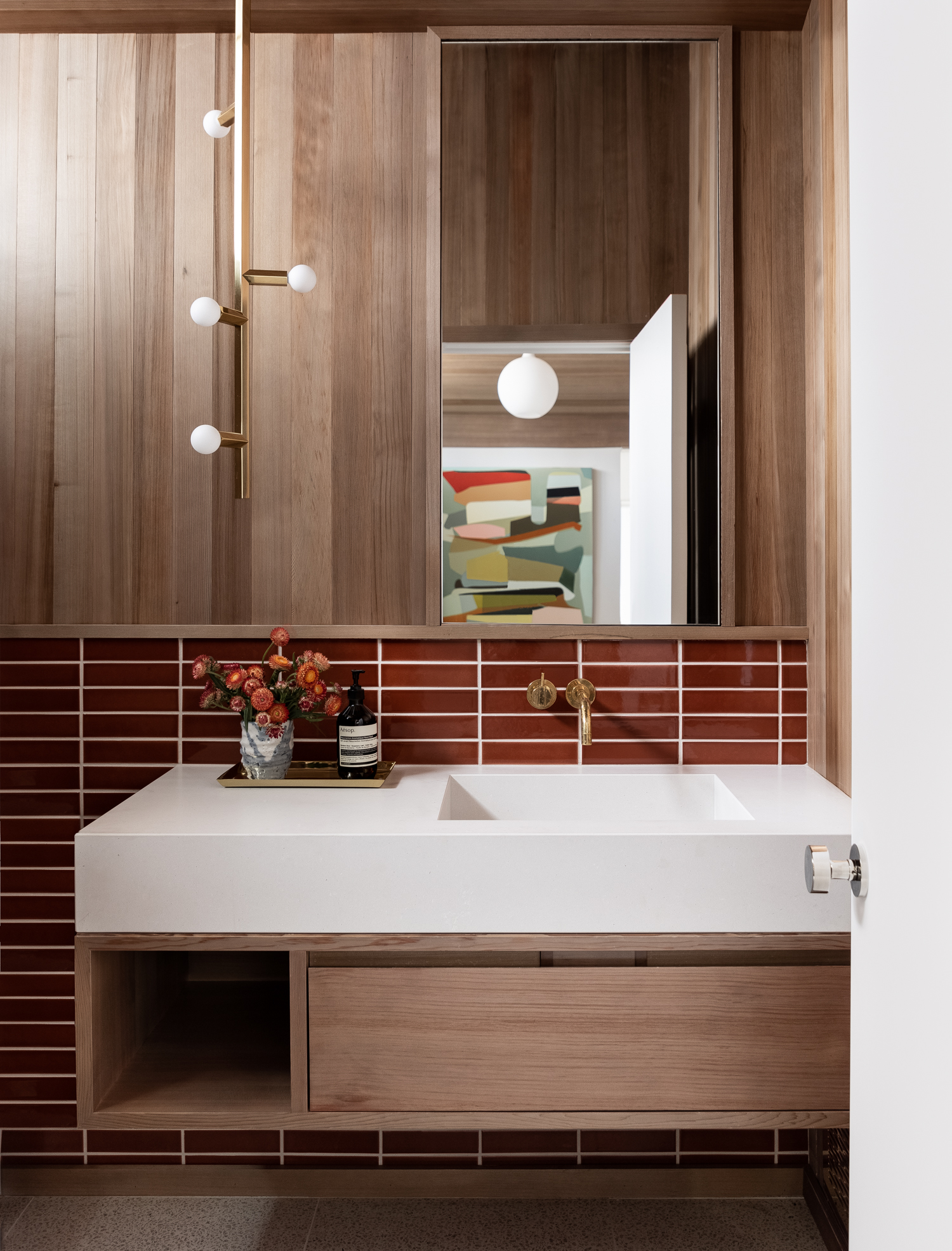 The powder room features a deep orange tile, brass finishes, and cedar cladding.