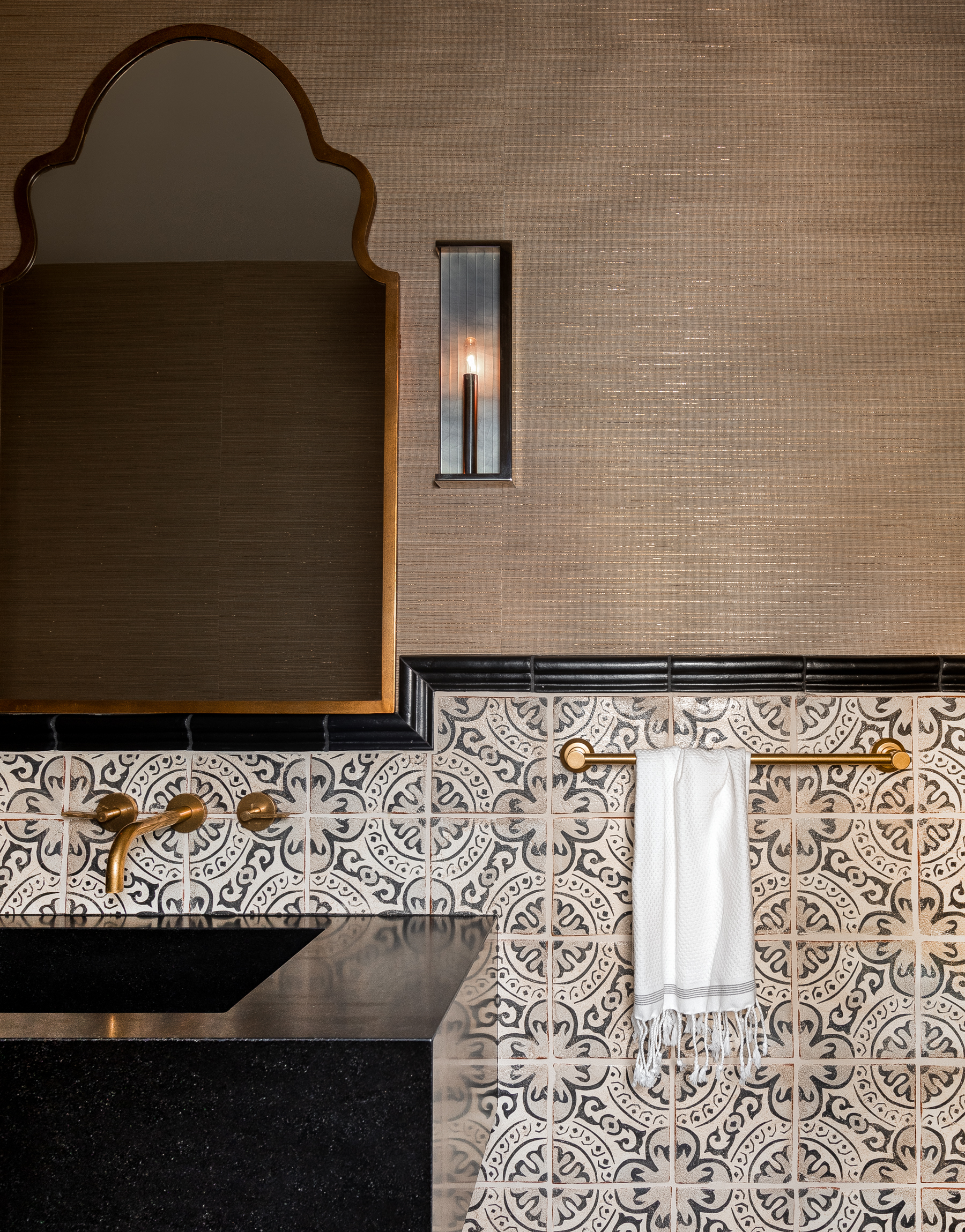 Powder room with Moroccan mirror in metal with antique gilt, Hartmann & Forbes wallcovering, sconces in heirloom finish, and an antique mirror, embodying a Moroccan and masculine aesthetic.