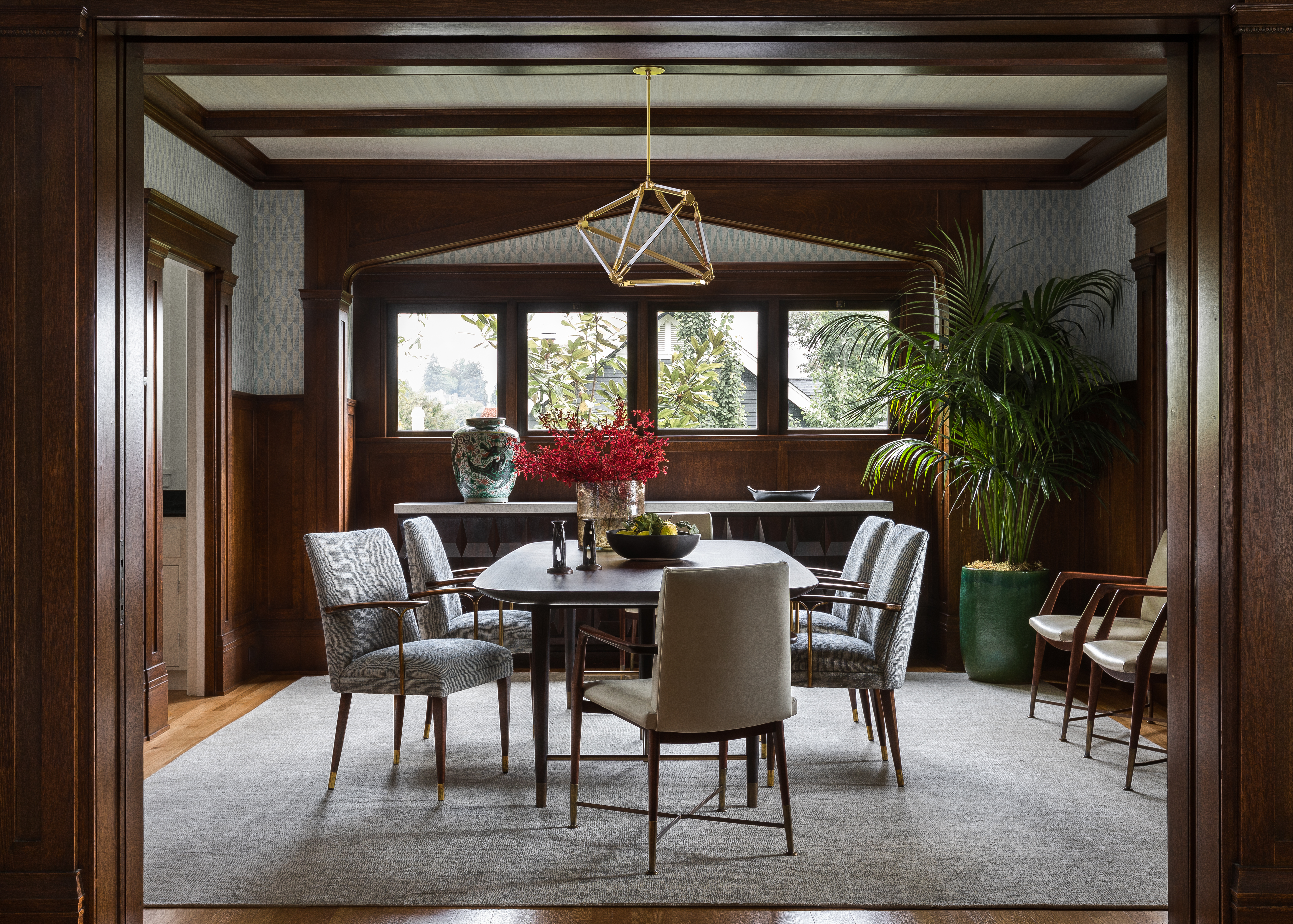 The dining room features patterned rice cloth walls and a custom walnut and brass dining table. Italian and Spanish midcentury chairs were reupholstered in leather and linen.