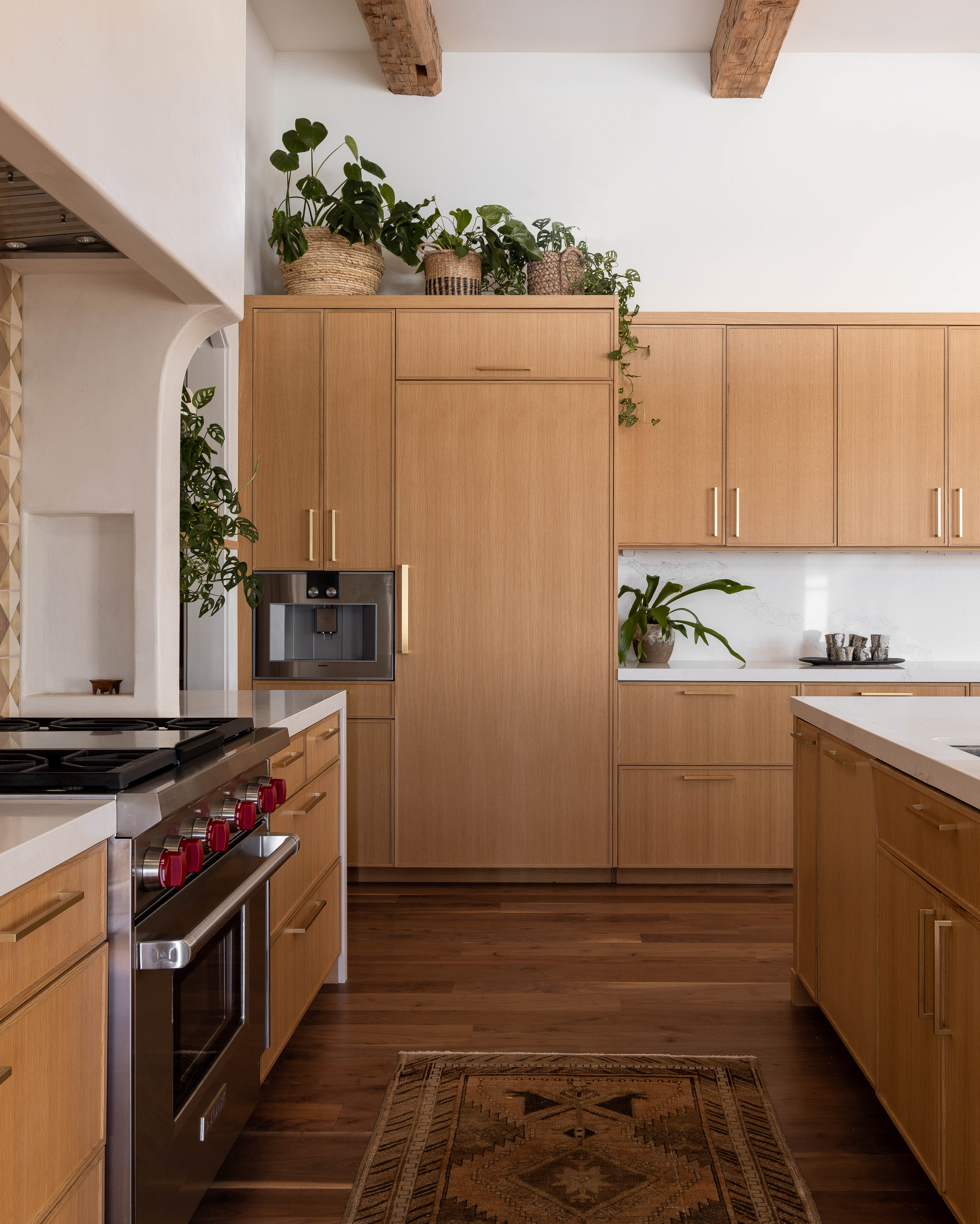 Stylish white oak-paneled fridge and wall of cabinets with brass hardware in a modern kitchen. California-cool design meets functionality