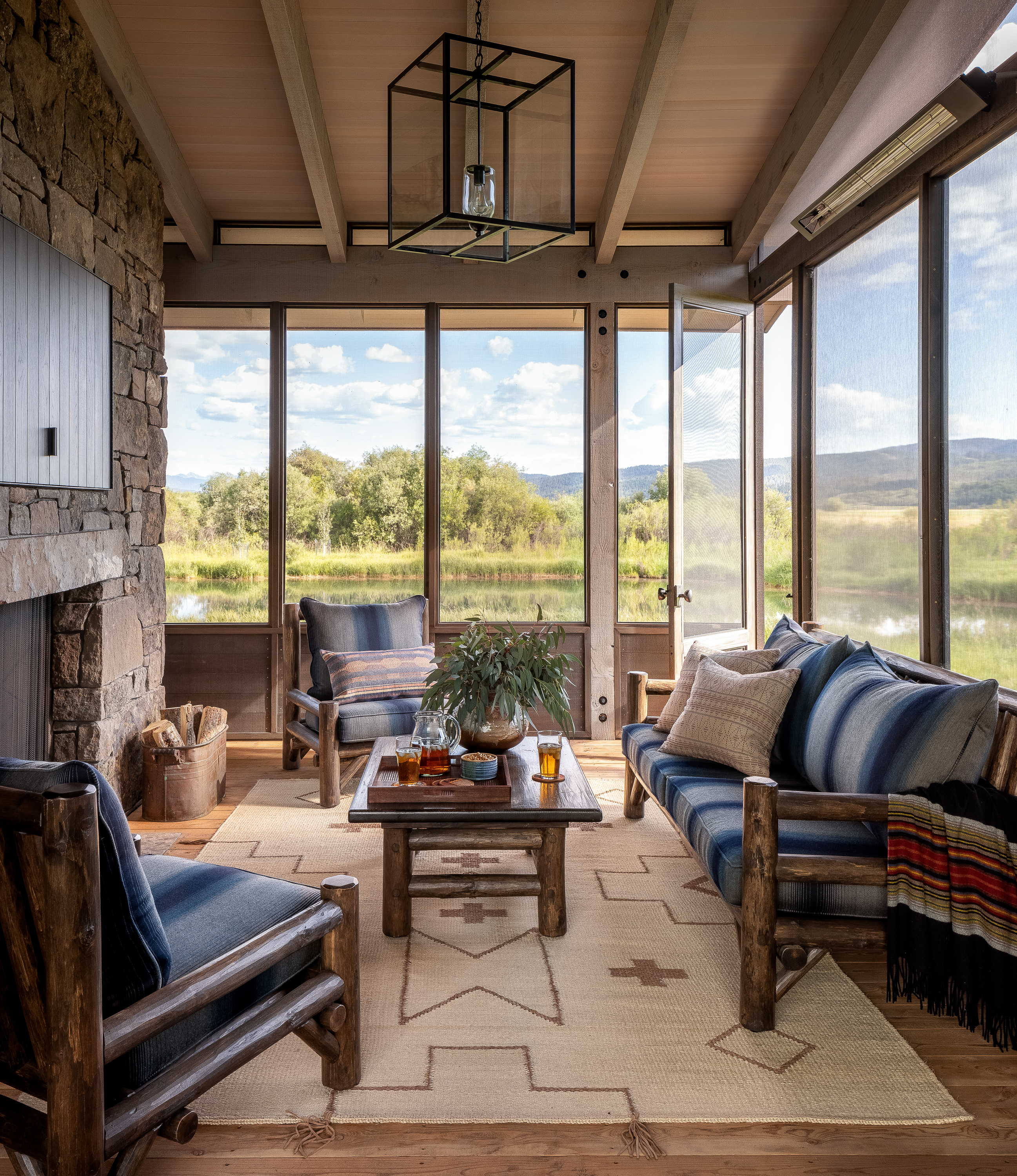 A sunlit log cabin-style sunroom with glass walls on three sides, showcasing exterior finishes indoors. A large fireplace shares the fourth wall, creating a cozy retreat