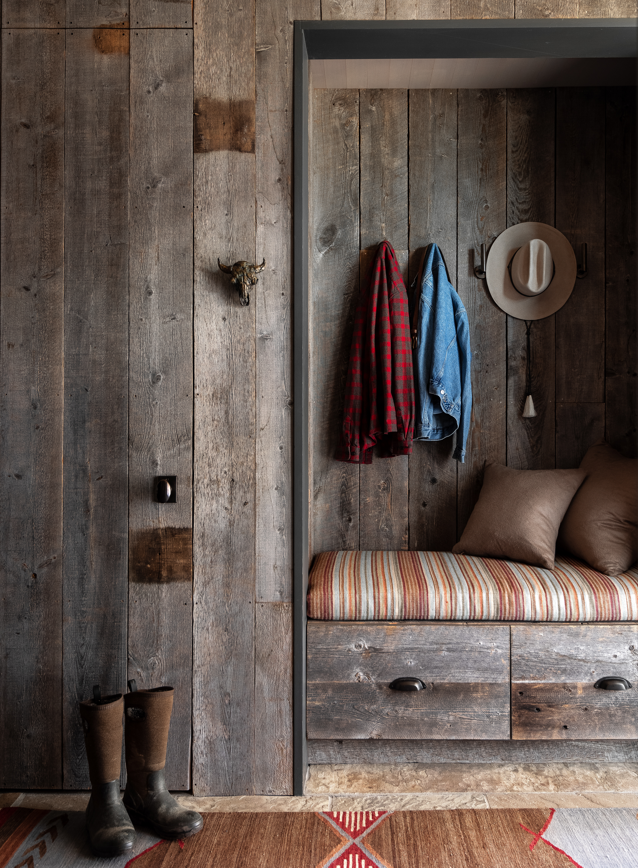 Detail shot of the mudroom featuring a built-in bench, cabinets for boots, plenty of hooks for coats, and a closet, all clad with the same reclaimed wood