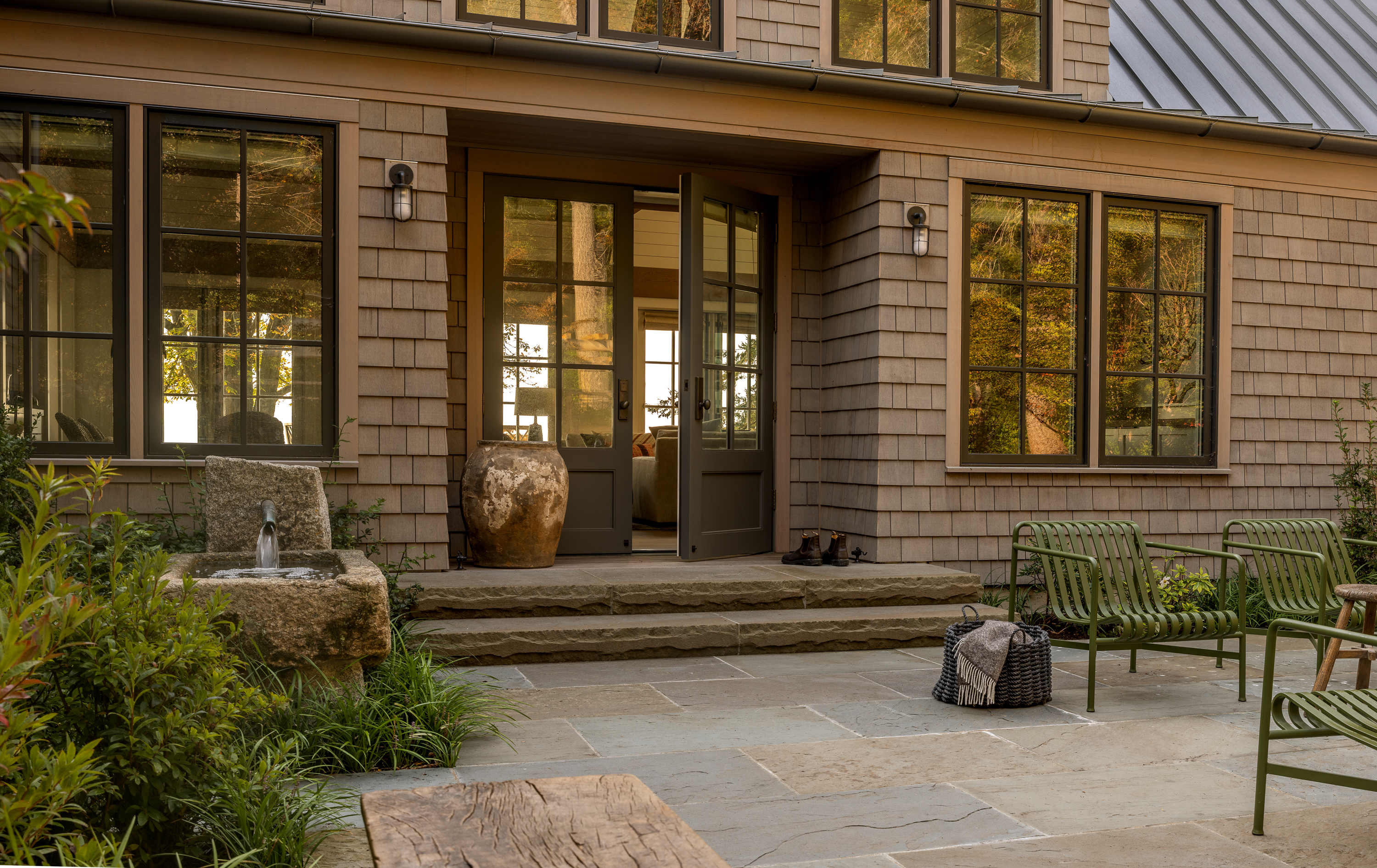 The main entry exterior features large stone steps, a water feature, and an open patio space, creating a welcoming and serene outdoor ambiance.