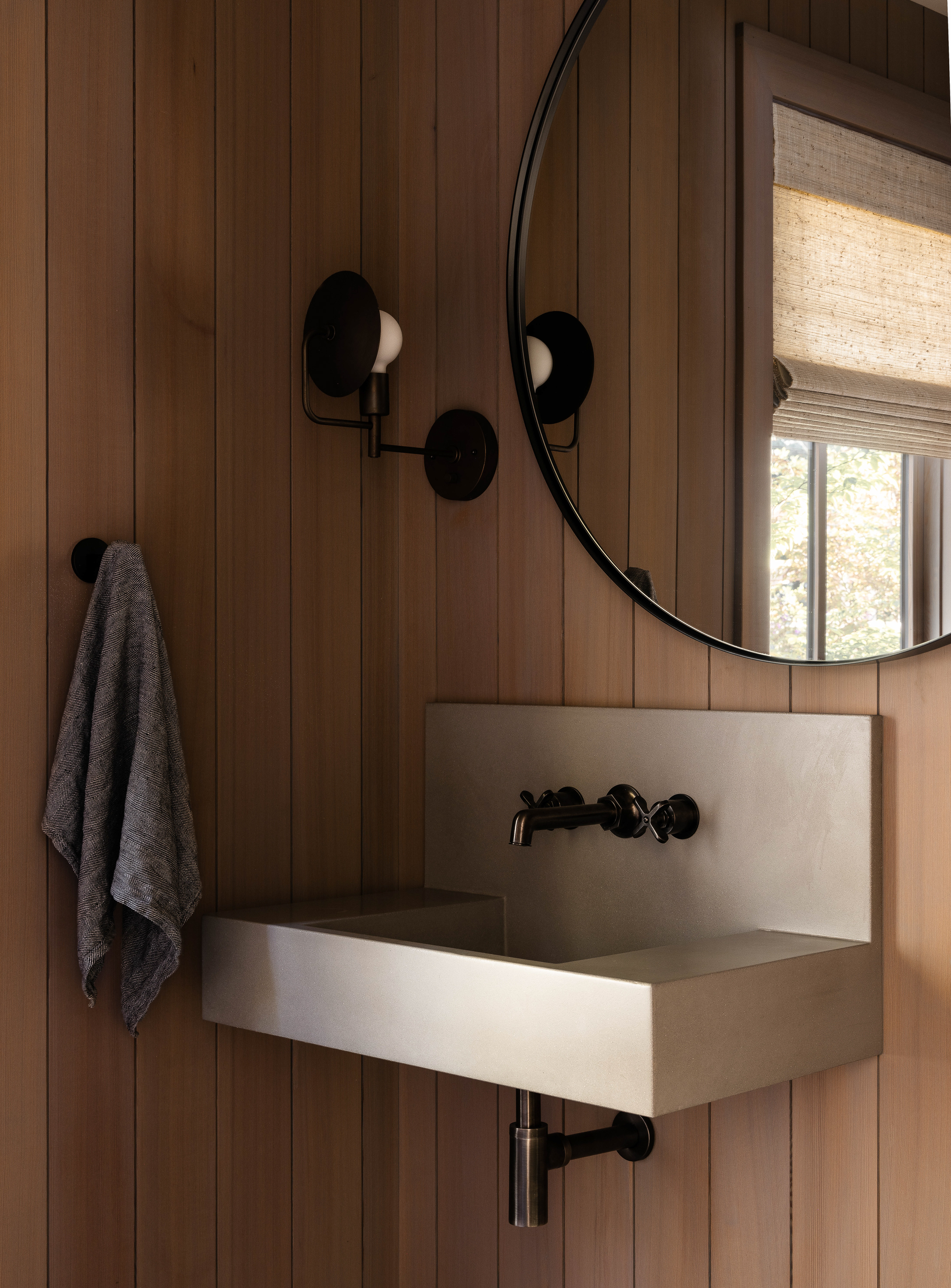 A close-up of the materials in the powder room reveals a honed concrete sink paired with light-stained vertical wood paneling and oil-rubbed bronze finishes, creating a modern yet warm ambiance.