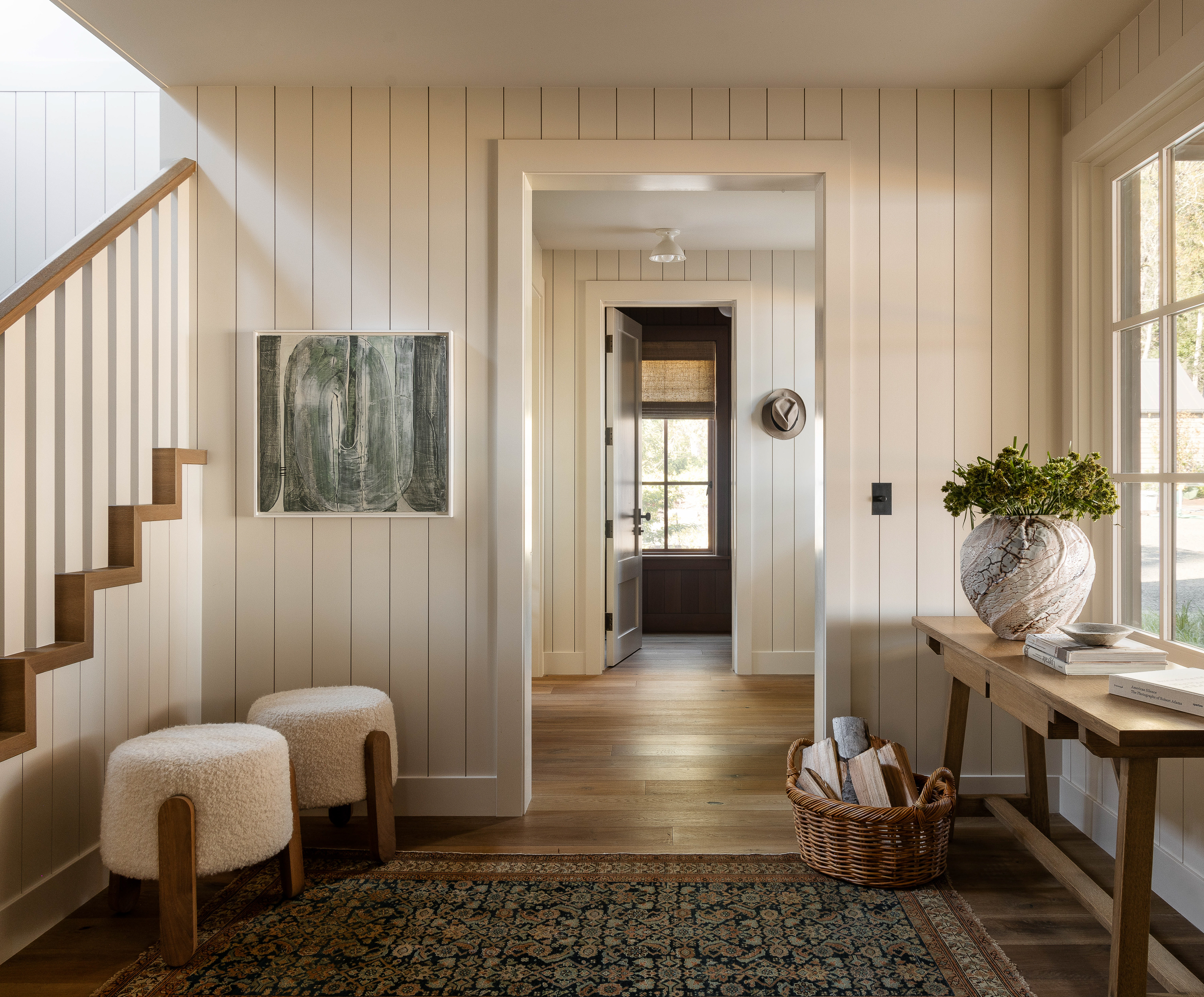 The entry foyer, bright and airy, becomes a central access point, with simple furnishings for a key drop and package storage. A dark Persian rug adds warmth and complements the family dog