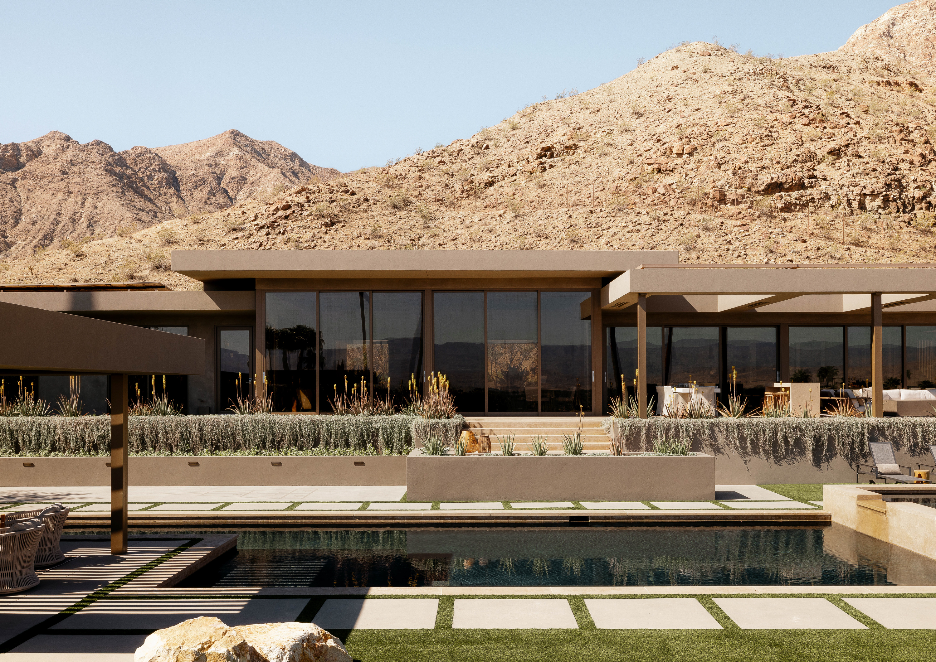 View of Palm Springs Retreat from across the pool: The house emerges elegantly, blending with the desert landscape, creating a harmonious and picturesque setting.