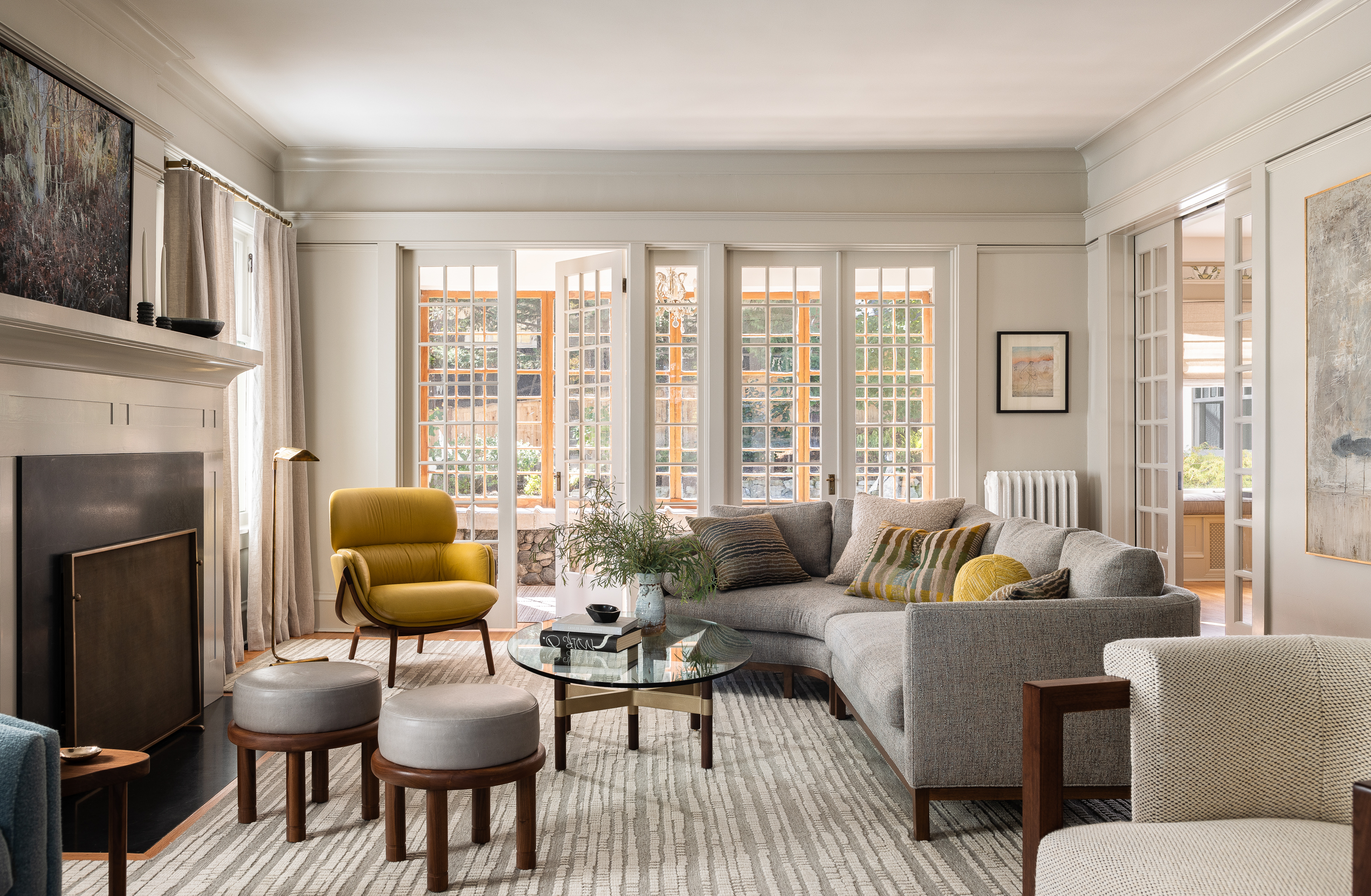 The living room features warm gray walls, contemporary furniture, and lighting for both formal and inviting ambience. Textures like leather, wool, and linen complement a hand-woven wool rug.