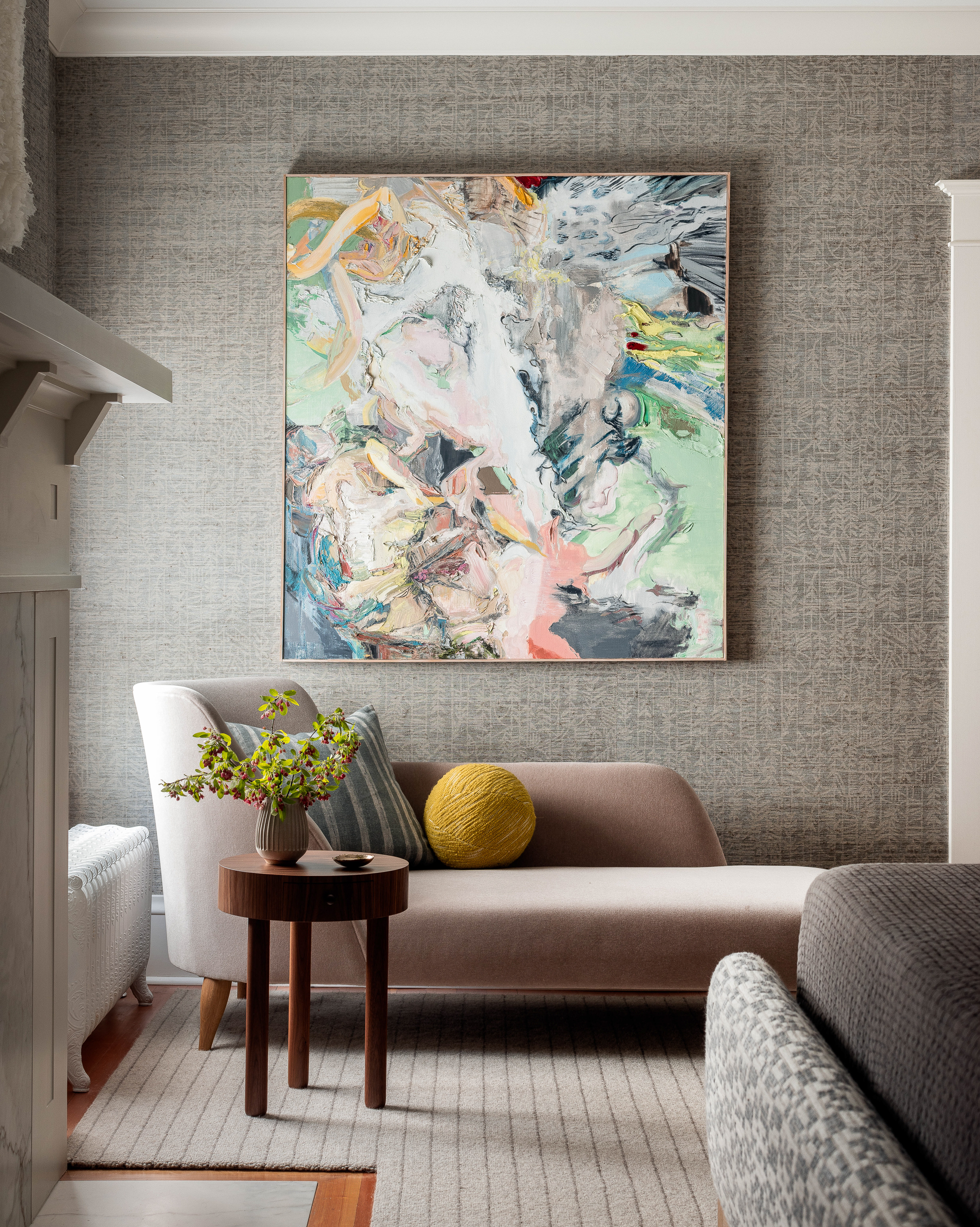 A light Pink upholstered chaise sits beneath a colorful oil painting by Drie Chapek.